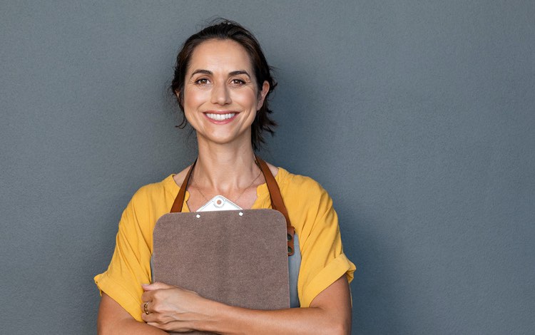 smiling worker wearing an apron and holding a clipboard